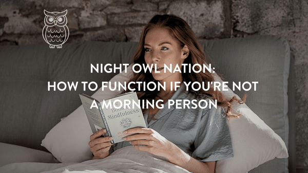 Person sitting up in bed reading a book at night with an owl to the right of her