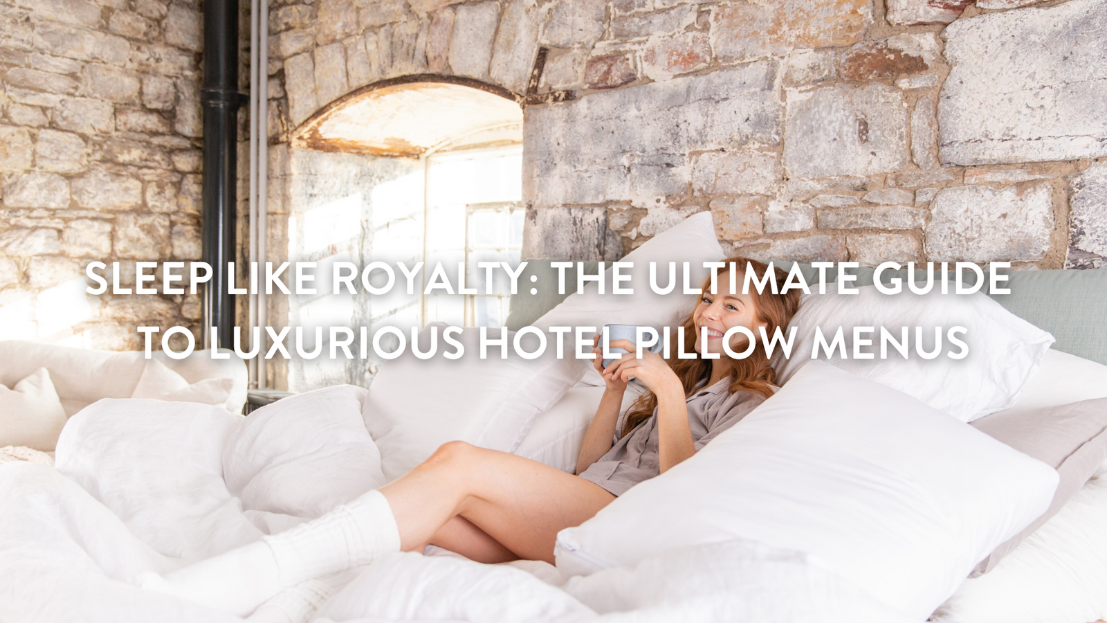 Person sitting up in bed drinking tea and surrounded by pillows 